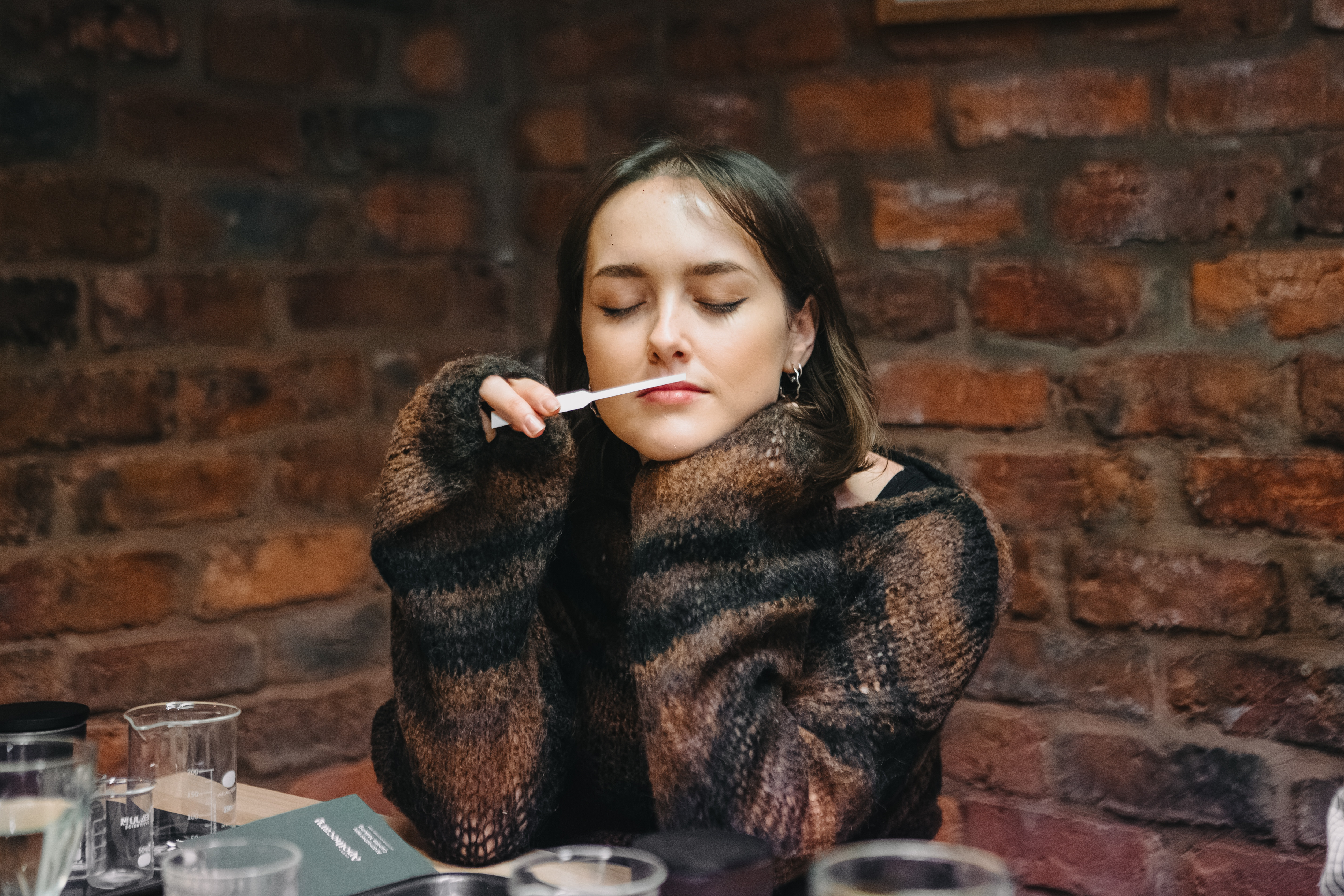 A woman is inhaling the essential oil scent on a tester stick with her eyes closed